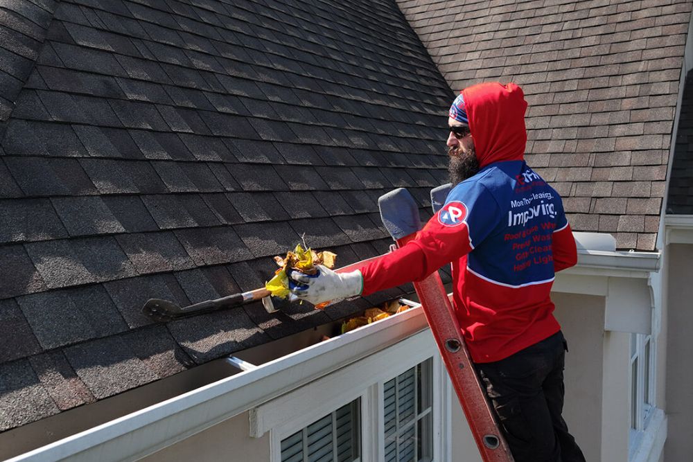 A man in a red and blue hoodie is engaged in roof work, focusing on gutter installation in Reno, NV.